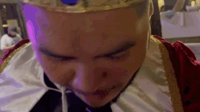 a man wearing a crown and a cape is eating something with a straw