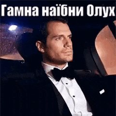 a man in a tuxedo and bow tie is sitting in the back of a car .