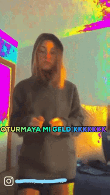 a woman in a hoodie stands in front of a colorful background with the words oturmaya mi geldikkkkkkk written on it