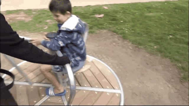 a little boy is riding a merry go round with a person holding his hand