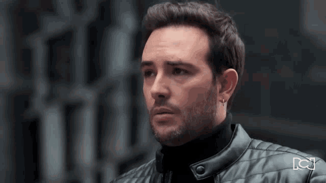 a man with a beard is wearing a black turtleneck and a leather jacket .