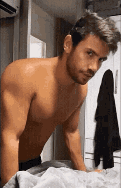 a shirtless man is standing on a bed with a blanket on it
