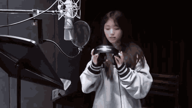 a girl is standing in front of a microphone holding a pair of headphones