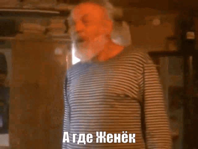 a man in a striped shirt is standing in front of a window and says " a где женек "