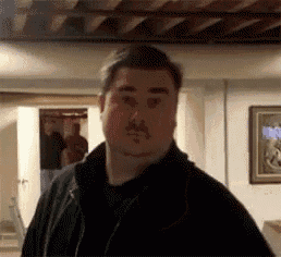 a man with a mustache is standing in a room in front of a picture .