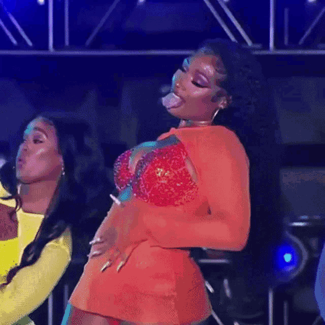 a woman in an orange dress is sticking her tongue out while dancing on stage .