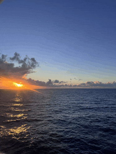 the sun is setting over the ocean with a blue sky