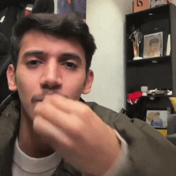 a man with a mustache is eating something in front of a shelf with the letter l on it