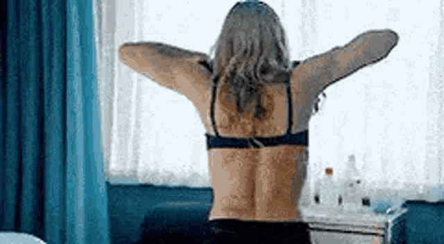 a woman in a bra is stretching her arms in front of a window in a hotel room .