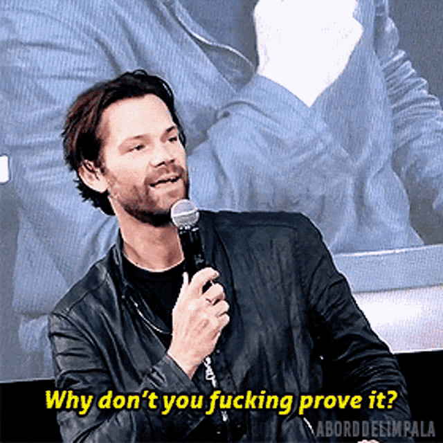 a man in a leather jacket is holding a microphone and saying why don t you fucking prove it