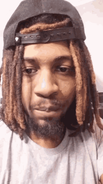 a man with dreadlocks is wearing a hat and a gray shirt