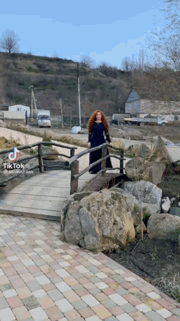 a woman in a blue dress is standing on a wooden bridge with tik tok written on the bottom right