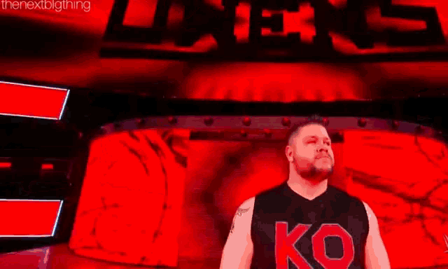 a kevin owens is standing in front of a large red screen .