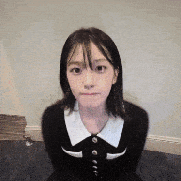 a girl in a black dress with white buttons on the collar looks at the camera