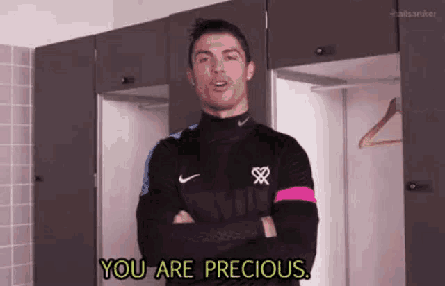 a soccer player is standing in a locker room with his arms crossed and saying `` you are precious '' to the camera .