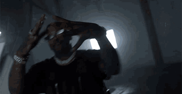 a man wearing sunglasses is standing in a dark room with a light behind him .