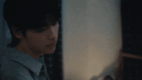 a man in a blue shirt is sitting in a dark room looking at something .