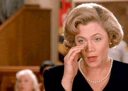 a woman with a pearl necklace wipes her nose