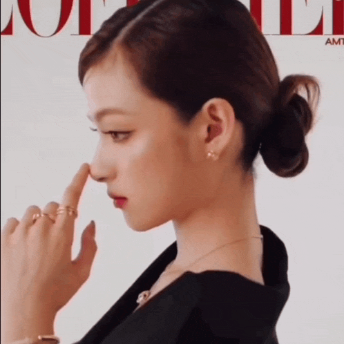 a woman with a bun on her hair is touching her nose in front of a vogue magazine cover