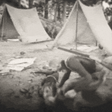 a black and white photo of a group of people laying on the ground in front of tents