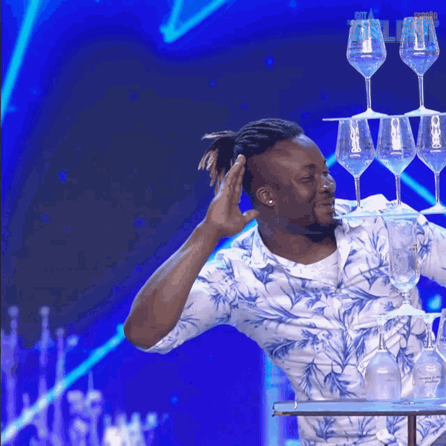 a man stands on a table with a stack of wine glasses on top