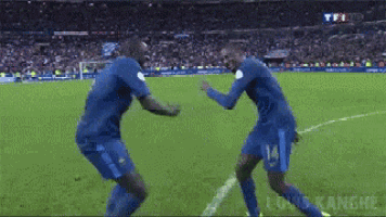 two soccer players are dancing on the field and one has the number 14 on his shirt