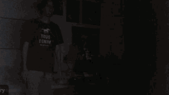 a man wearing a true denim shirt stands in the dark