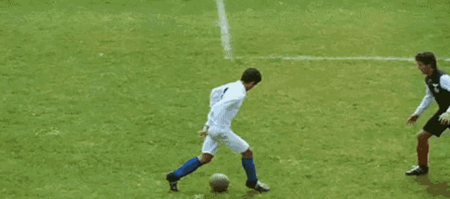 a soccer player kicking a soccer ball on a field while another player watches .