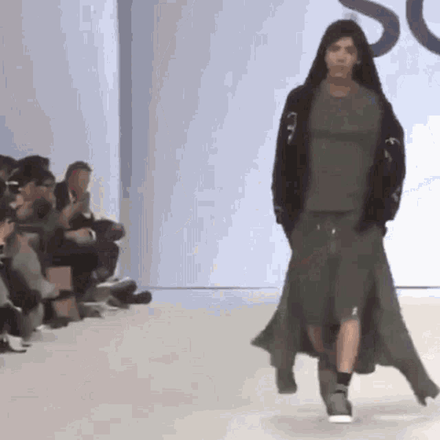 a model walks down the runway at a fashion show while a crowd watches