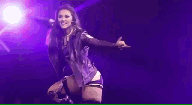 a woman is dancing on a stage with her arms outstretched in front of a purple light .