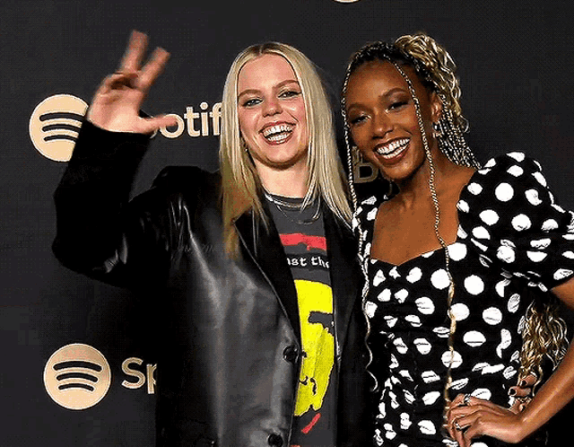 two women are posing for a picture in front of spotify logos