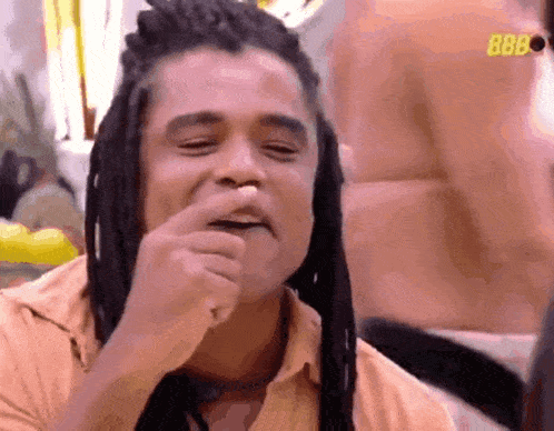 a man with dreadlocks is making a funny face and covering his mouth with his hand .