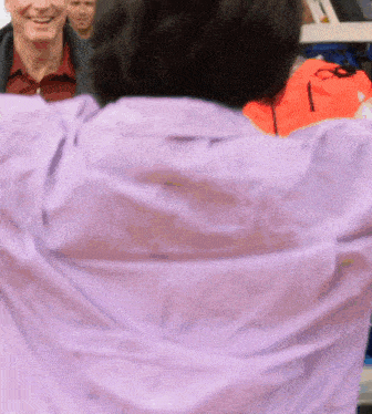 a man in a purple shirt is smiling in front of a group of men
