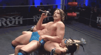 a wrestler is holding a microphone while laying on another wrestler 's back