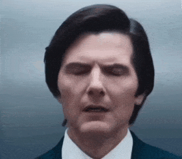 a man in a suit and tie is making a funny face with his eyes closed .
