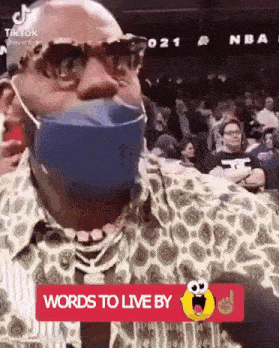 a man wearing a mask and glasses is sitting in a crowd at a basketball game .