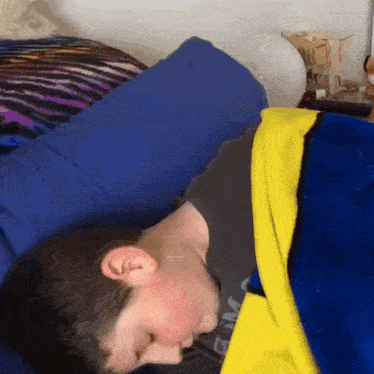 a boy is laying in bed with a blue blanket and a yellow blanket