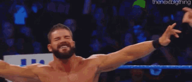 a man with a beard is standing in a wrestling ring with his arms outstretched and laughing .