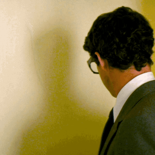 a man wearing glasses and a suit looks down at something