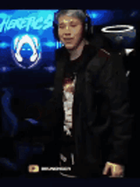 a man wearing headphones and a black shirt is standing in front of a screen .