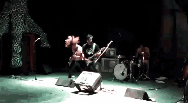 a man is playing a guitar on a stage with a drum set .