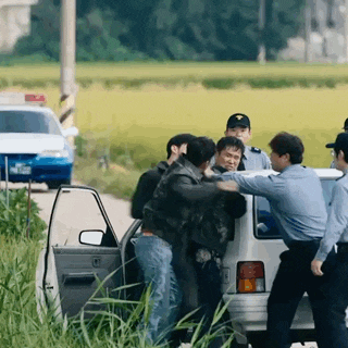 a group of police officers are standing around a car holding a man .