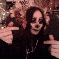 a woman with a skull face paint and a crown on her head giving a thumbs up