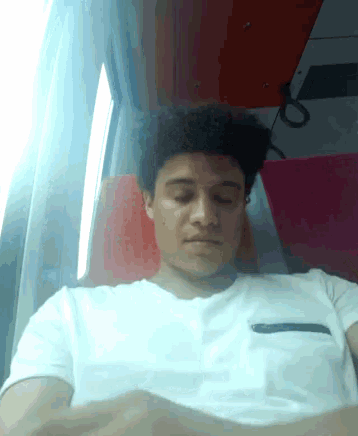 a man in a white shirt is sleeping on a train