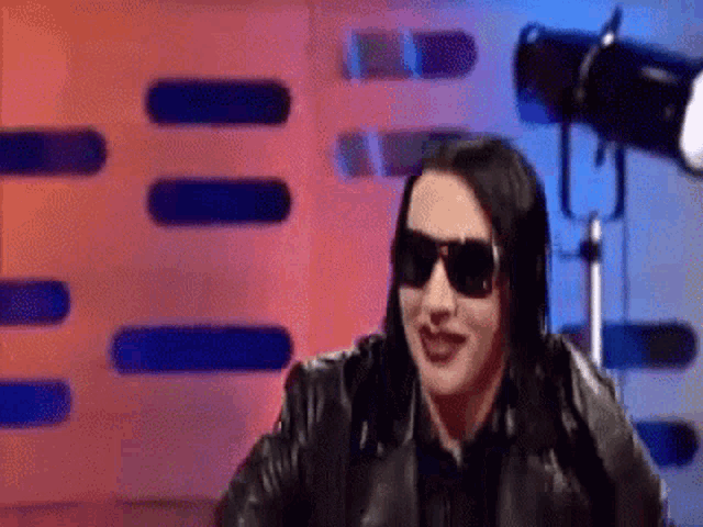a woman wearing sunglasses and a leather jacket is smiling .