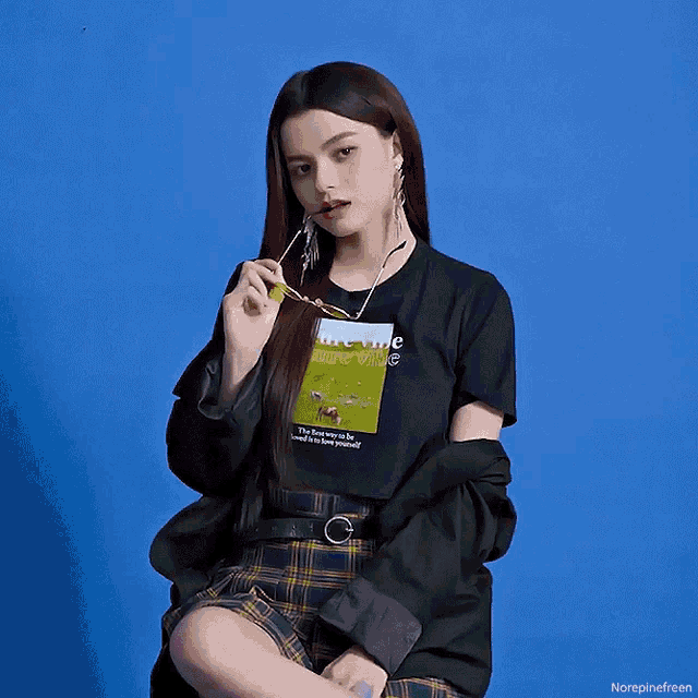 a girl wearing a blue shirt that says " the best thing to be yourself is to be yourself " is sitting in front of a blue wall
