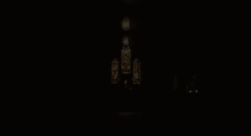 a woman stands in a dark room with candles and a stained glass window