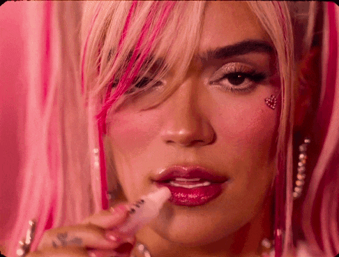 a woman with pink hair is applying lip gloss