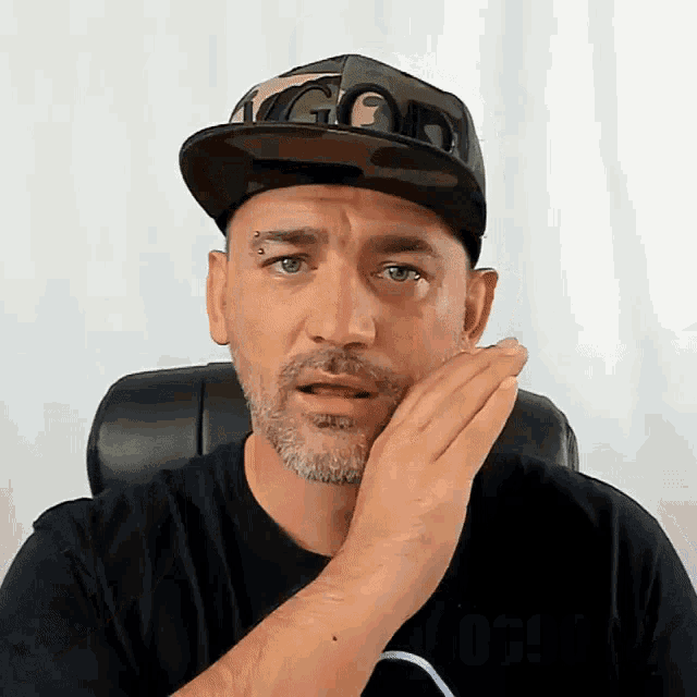 a man wearing a black shirt and a camo hat with the word god on it