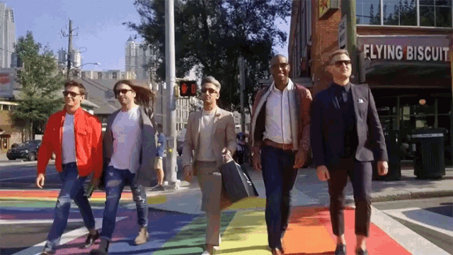 a group of men walk across a rainbow colored crosswalk in front of flying biscuit